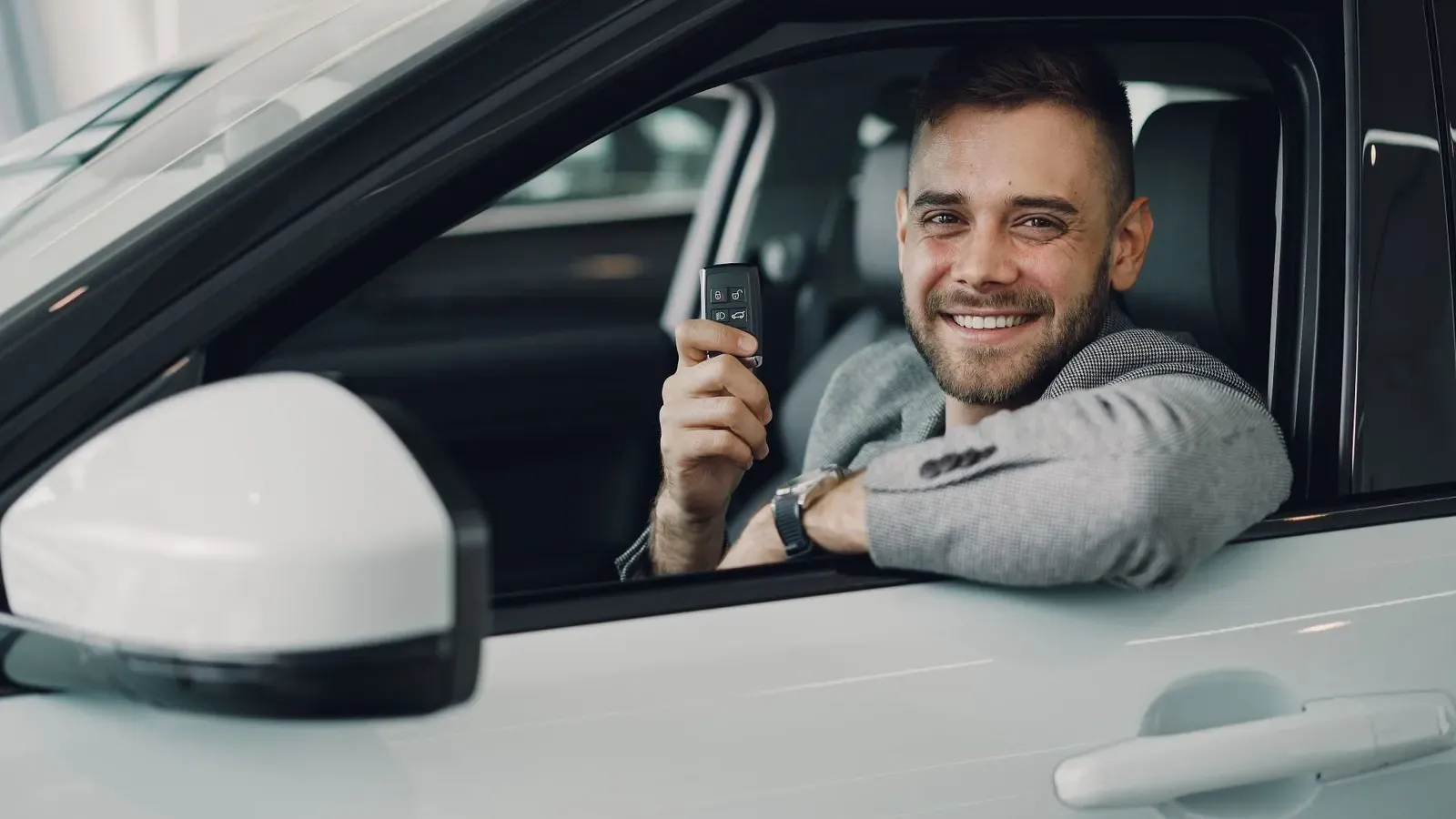 Mann hält im Auto lächelnd seinen Schlüssel in die Kamera